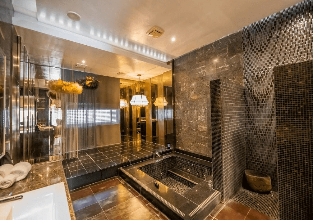 【員林住宿】楓采時尚汽車旅館沉穩奢華的浴室空間，黑色大理石與金色燈光營造低調奢華感。浴池採用黑色石材，搭配金屬質感的牆面裝飾與間接燈光設計，提升整體空間的高級感與舒適度。