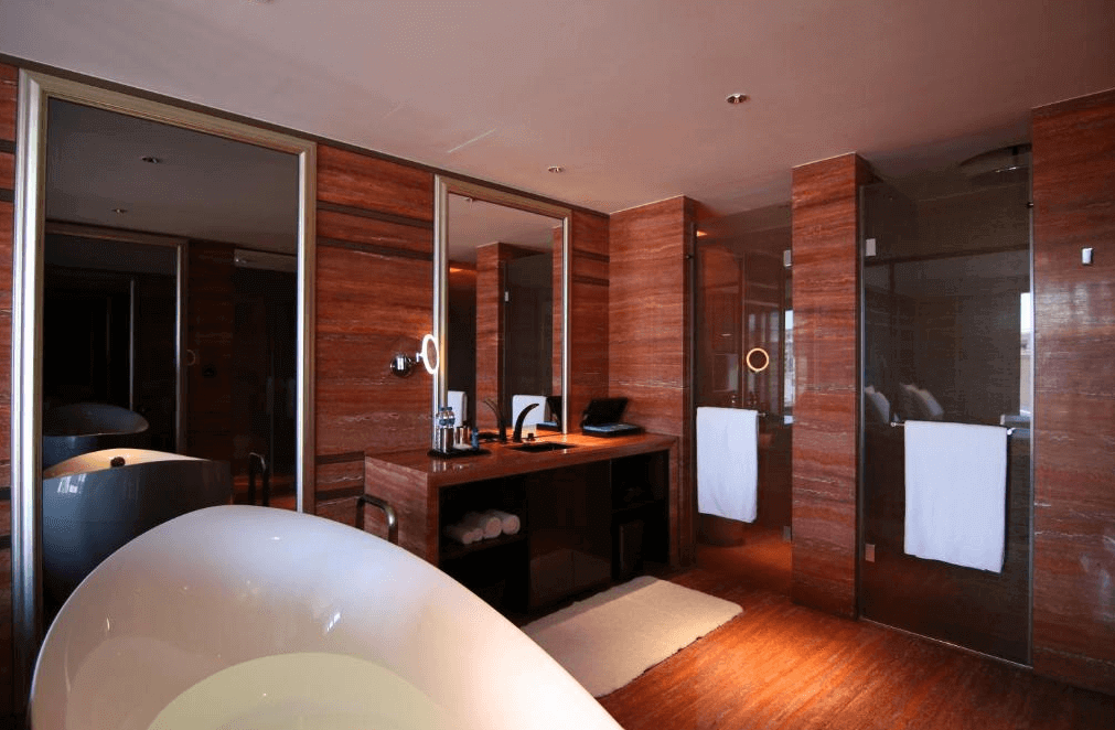 【高雄親子飯店】水京棧國際酒店高級感十足的衛浴空間，以木質紋理為主題，搭配鏡面元素，呈現摩登質感。房內設有獨立圓形浴缸、雙人洗手台與玻璃隔間淋浴間，整體設計典雅且富有層次感，營造頂級飯店的奢華享受。