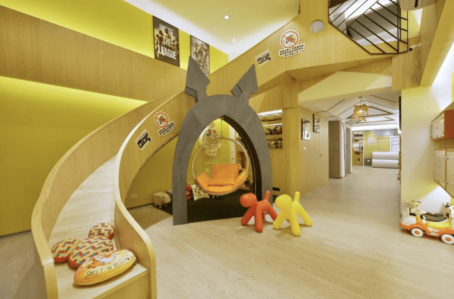 【台南安平住宿】溜小孩親子民宿充滿童趣的親子遊戲空間設有木質溜滑梯與拱門造型入口，中央為透明懸掛吊椅搭配橘色抱枕，四周妝點各式趣味裝飾與標語，營造出如同兒童樂園般的玩樂天地，適合孩童奔跑與探索。