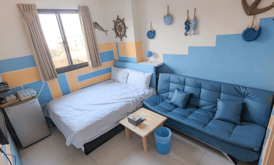 【虎尾住宿】澐河民宿的海洋風格主題客房，牆面以藍橘配色，房內設有雙人床與深藍色沙發，裝飾有海星、舵輪與海馬等海洋元素，整體氛圍溫馨且富有童趣。