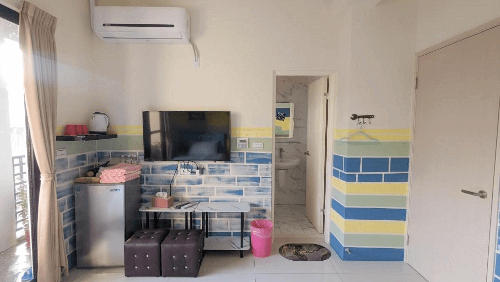 【虎尾住宿】澐河民宿的客房一隅展示，牆面以彩色磚塊風格裝飾，設有電視、冰箱、茶水區與毛巾架，旁邊為通往浴室的門口，整體空間充滿童趣與實用設計感。