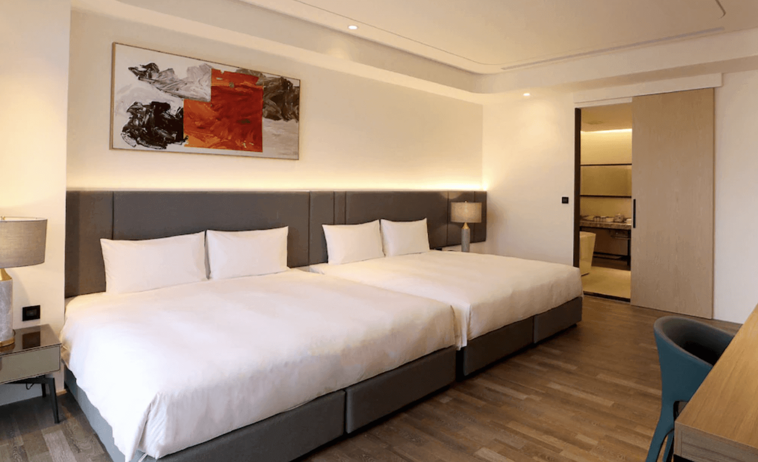 【台南安平住宿】福爾摩沙遊艇酒店的四人家庭房，配有兩張大床與溫潤木地板，牆面掛有抽象畫作並以間接燈光營造柔和氛圍，房內設有書桌與滑門連接另一空間，適合親子與多人入住。