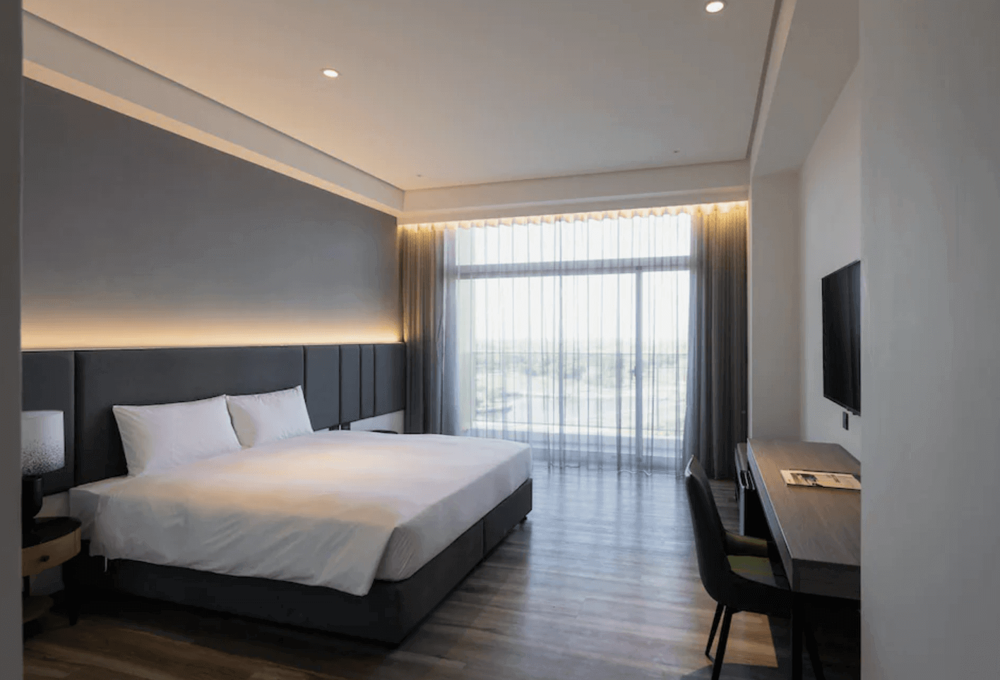 【台南安平住宿】福爾摩沙遊艇酒店的高樓層海景雙人房，設有一張大床與大片落地窗，可欣賞窗外自然景觀，房內以深灰與白色調為主，搭配簡約書桌與電視，空間寬敞明亮。