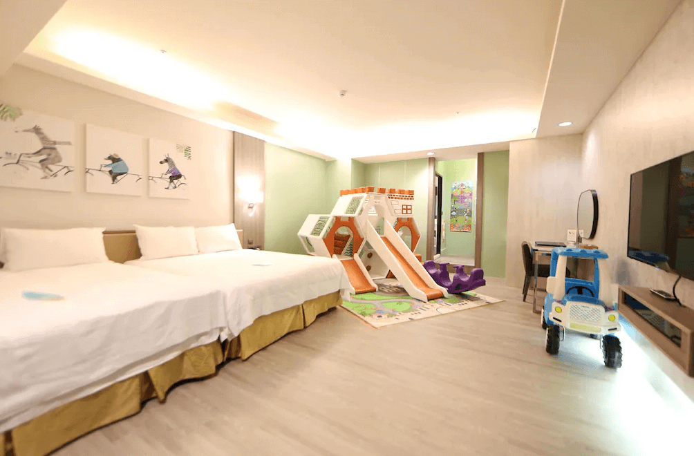 【斗六住宿】緻麗伯爵酒店的親子主題客房，配有兩張大床與大型室內滑梯組、搖搖馬與兒童電動玩具車，牆面裝飾童趣插畫，適合家庭旅客帶小朋友一起入住，提供舒適又有趣的住宿體驗。