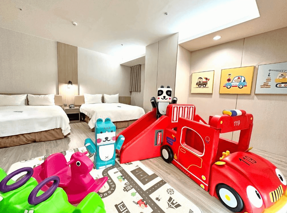 【斗六住宿】緻麗伯爵酒店的兒童主題房型，房內設有兩張雙人床與紅色消防車造型溜滑梯，以及多樣化兒童遊樂設施，地面鋪設道路圖案遊戲墊，整體氛圍活潑溫馨。