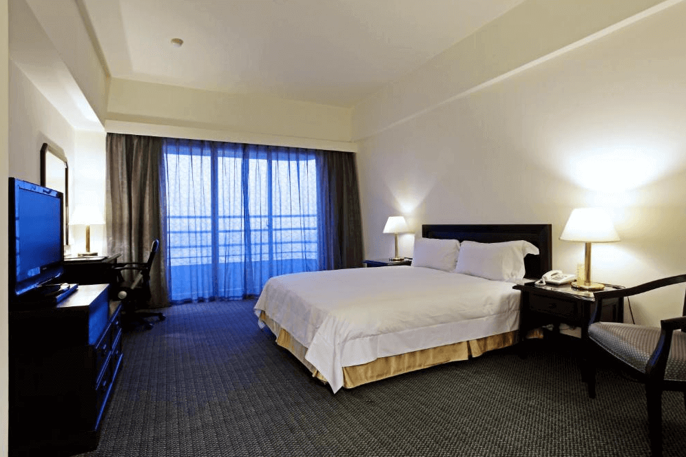 【斗六住宿】華安大飯店的雙人房空間，配有一張大床與辦公桌椅，窗前有落地窗簾與陽台，整體裝潢簡約舒適，以柔和燈光營造溫馨氛圍，適合商務或旅遊住宿。