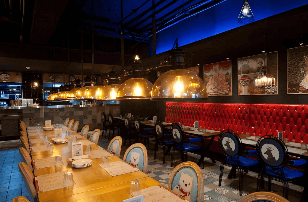 【虎尾住宿】虎尾春秋文創設計旅店的餐廳空間，搭配長型木桌與童趣圖案椅子，吊燈設計獨特，牆面掛有藝術畫作，紅色皮革沙發與藍色椅子相互呼應，營造出活潑且溫馨的用餐氛圍。