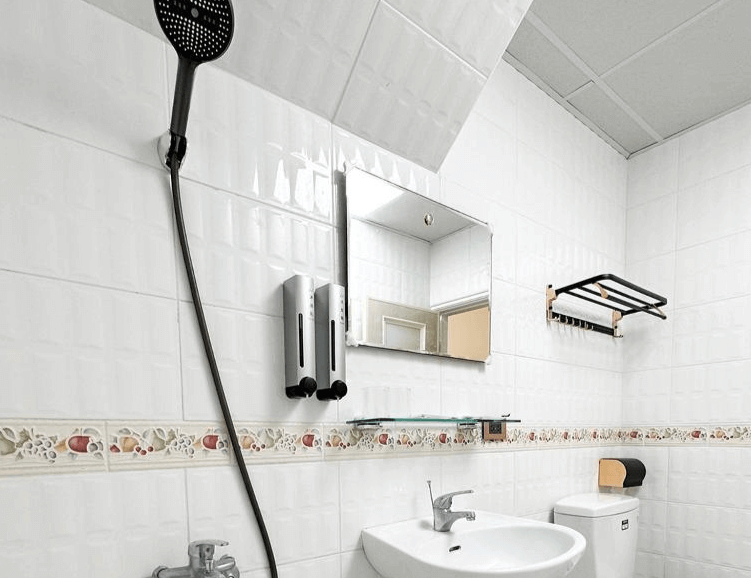 【虎尾住宿】虎尾漫遊的傳統風格浴室空間，白色磁磚牆面搭配水果花邊設計，設有洗手台、馬桶與掛壁式淋浴設備，簡約清爽且維持良好整潔。