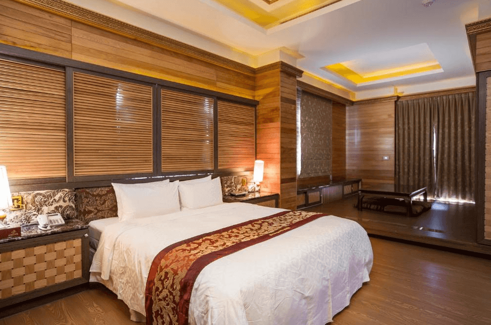 【斗六住宿】觀月商務休閒旅館的和風簡約設計的雙人房，房內鋪設木質地板與木質牆面，搭配百葉窗與溫暖燈光，大型雙人床鋪上鋪有東方風格織帶，房內設有獨立起居區，空間寬敞舒適。