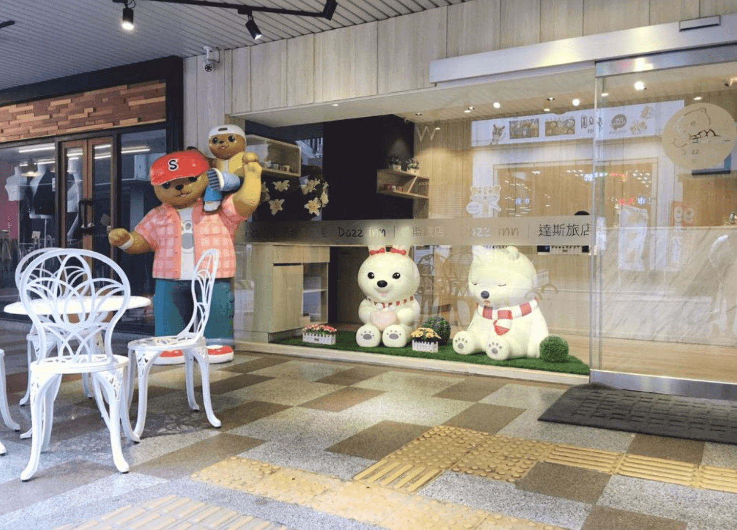 【逢甲夜市住宿】達斯旅店入口處設有可愛的熊主題裝飾與繽紛卡通人偶,外部環境明亮整潔,搭配戶外白色桌椅,打造出童趣溫馨的迎賓氣息,特別適合家庭旅客。