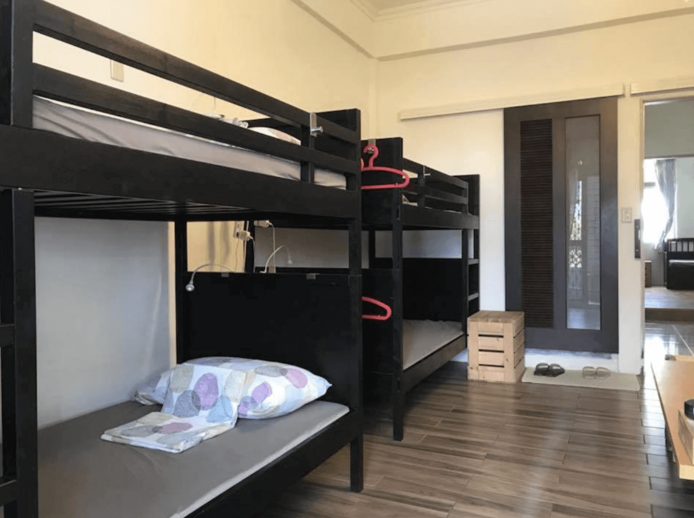 【鹿野住宿】鹿野結米家的宿舍房型，黑色木製床架搭配灰色床墊，設計簡潔大方。每個床位都配有掛勾、獨立閱讀燈和電源插座，提供個人化的住宿體驗。房內採用木地板，並設有滑門通往另一個房間，空間運用靈活。