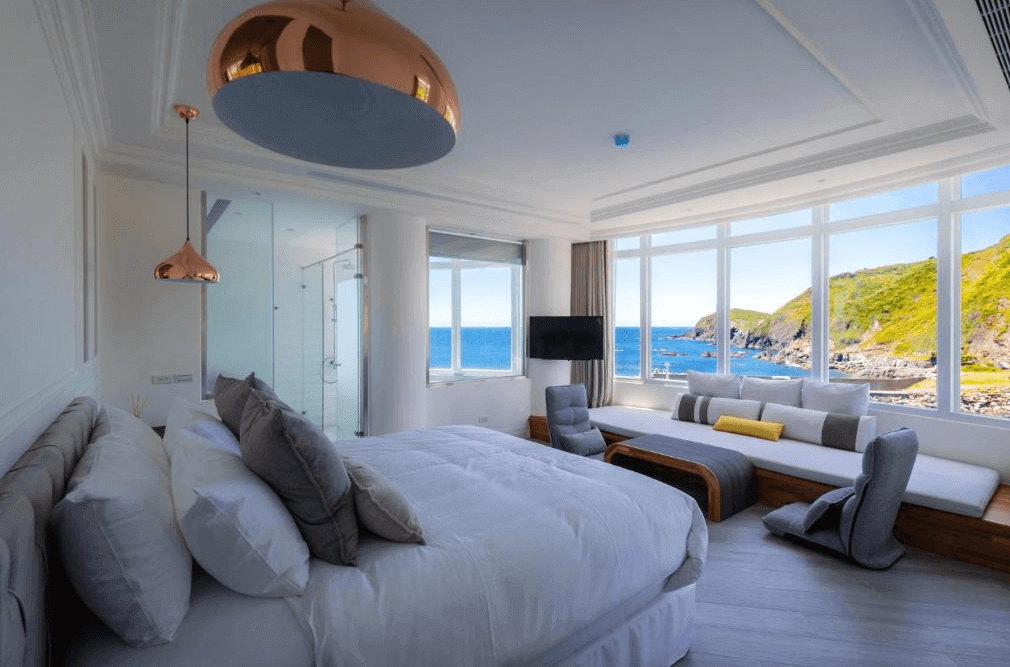 【蘇澳住宿】BRIGHTHOUSE 光之旅的海景雙人房，擁有大片落地窗可眺望湛藍海岸與綠意山崖，房內配有現代感吊燈、柔和色系床鋪與和風榻榻米座椅，設計簡約優雅。