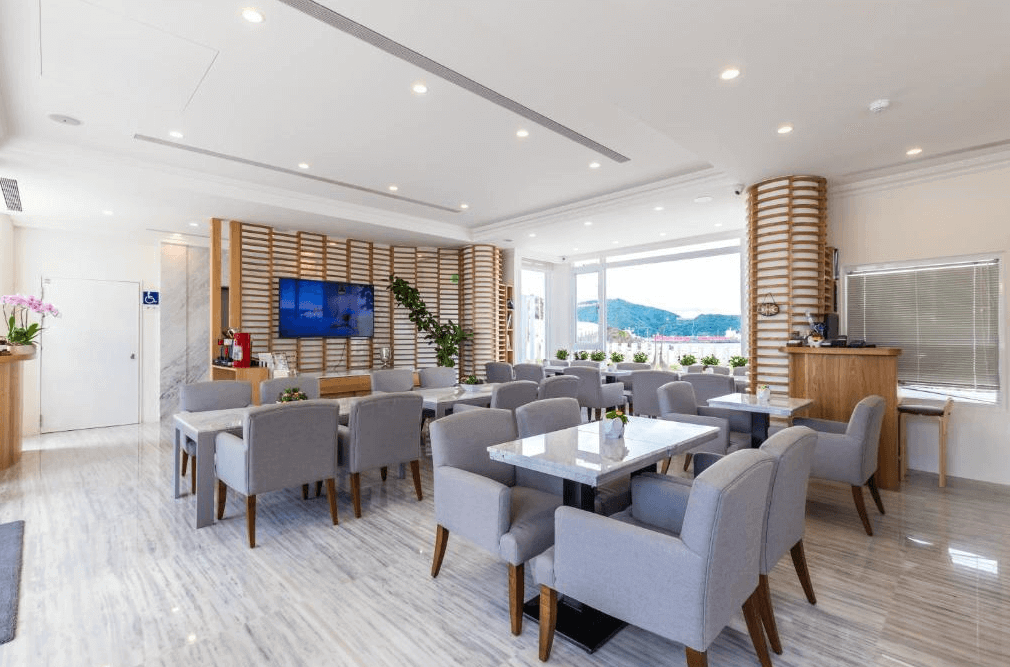 【蘇澳住宿】BRIGHTHOUSE 光之旅的公共交誼廳與早餐餐廳空間，設有多組灰色布椅與大理石桌，牆面搭配木質格柵與綠植裝飾，空間寬敞舒適，窗外可見山景。