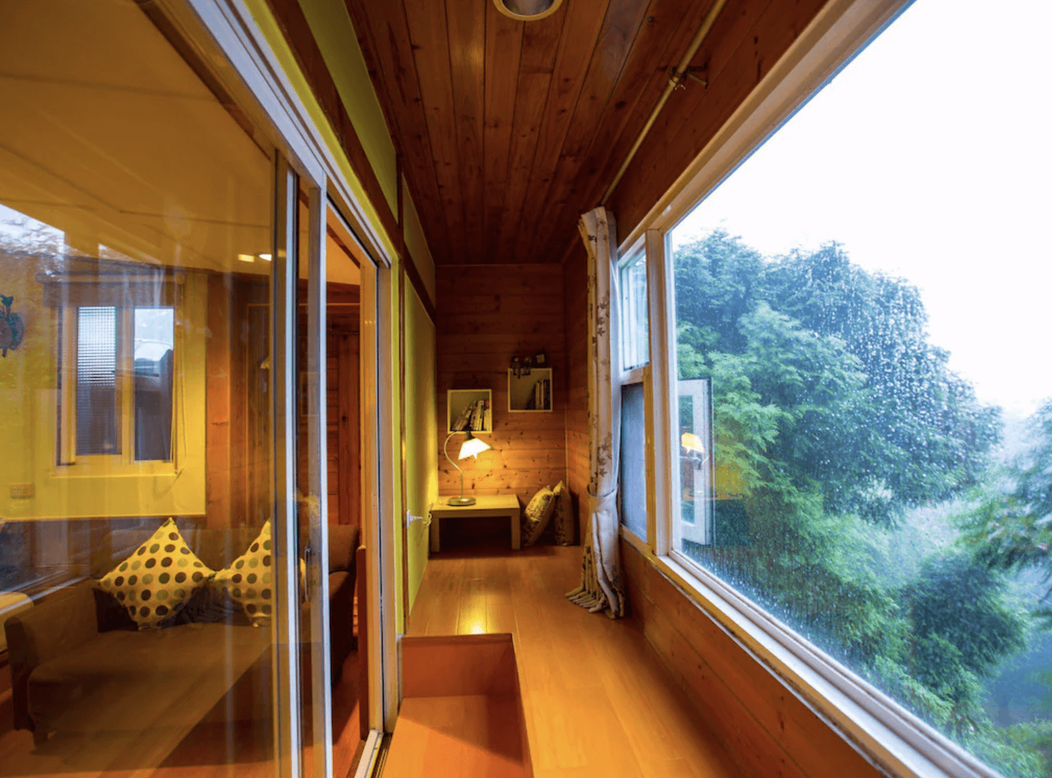 【清境農場住宿】五里坡民墅的木質走廊，大片玻璃窗外即是翠綠森林景色，走廊盡頭設有閱讀燈與坐墊空間，適合靜心放鬆或閱讀。室內以木頭元素為主，營造出與自然融合的靜謐氛圍。