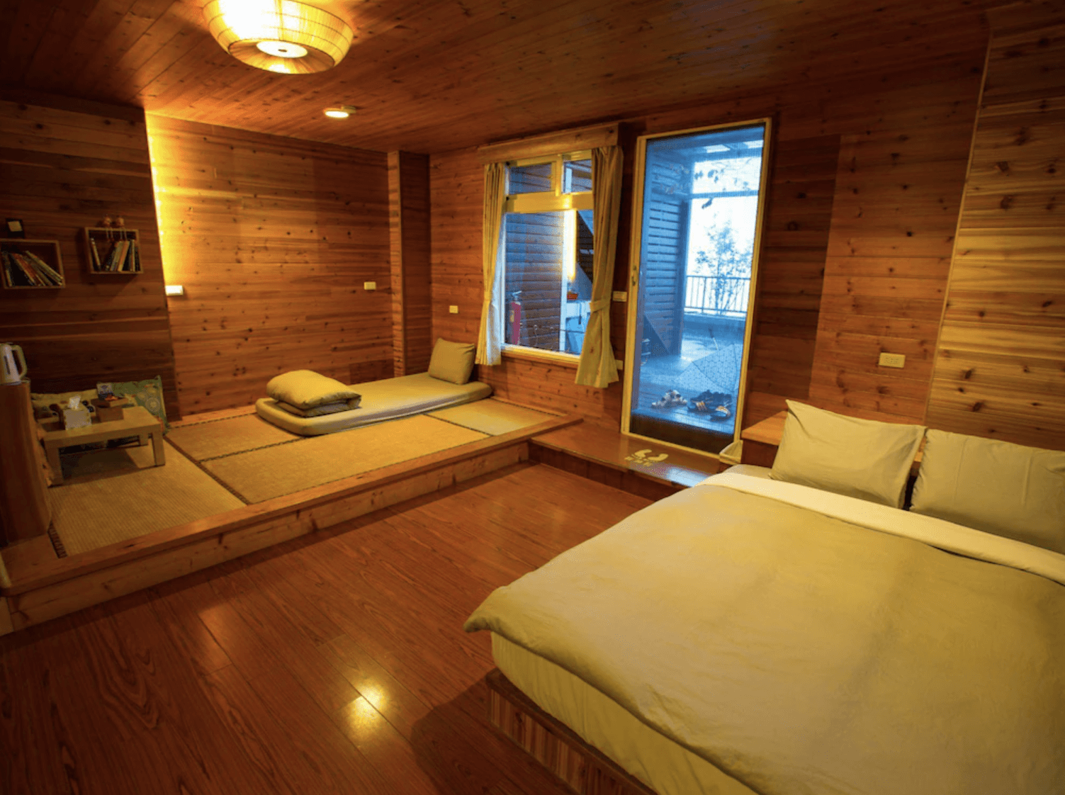 【清境農場住宿】五里坡民墅融合日式塌塌米與西式床鋪的溫馨房型，牆面與地板皆為原木設計，房內設有泡茶區與坐墊區，搭配暖色燈光與窗外景致，呈現質樸悠閒的山林生活風格。