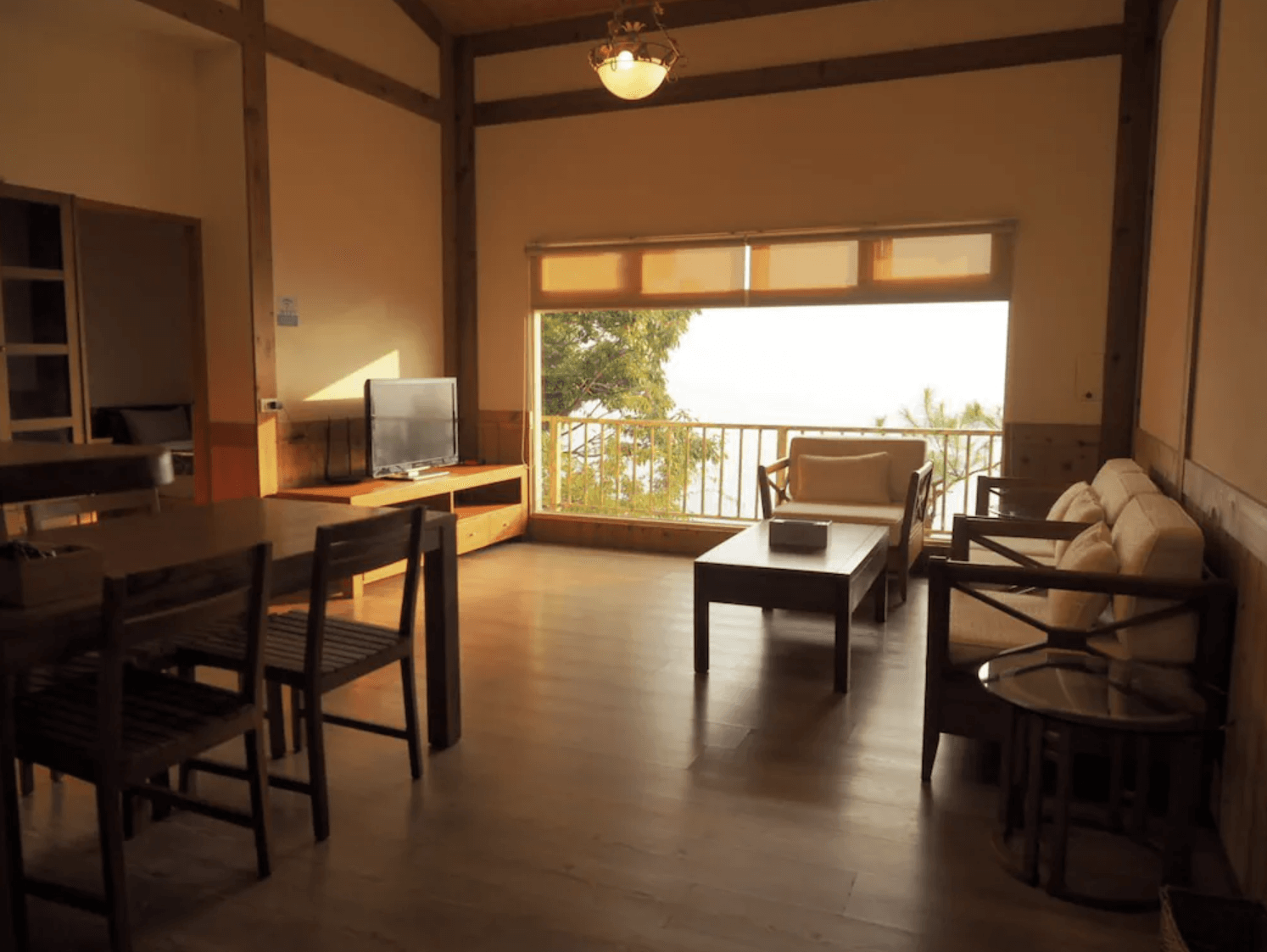 【清境農場住宿】五里坡民墅的客廳空間，配有木質餐桌椅與沙發組，大片窗戶可欣賞山林景致，室內光線柔和，裝潢簡約自然，適合團體旅客共度悠閒時光。