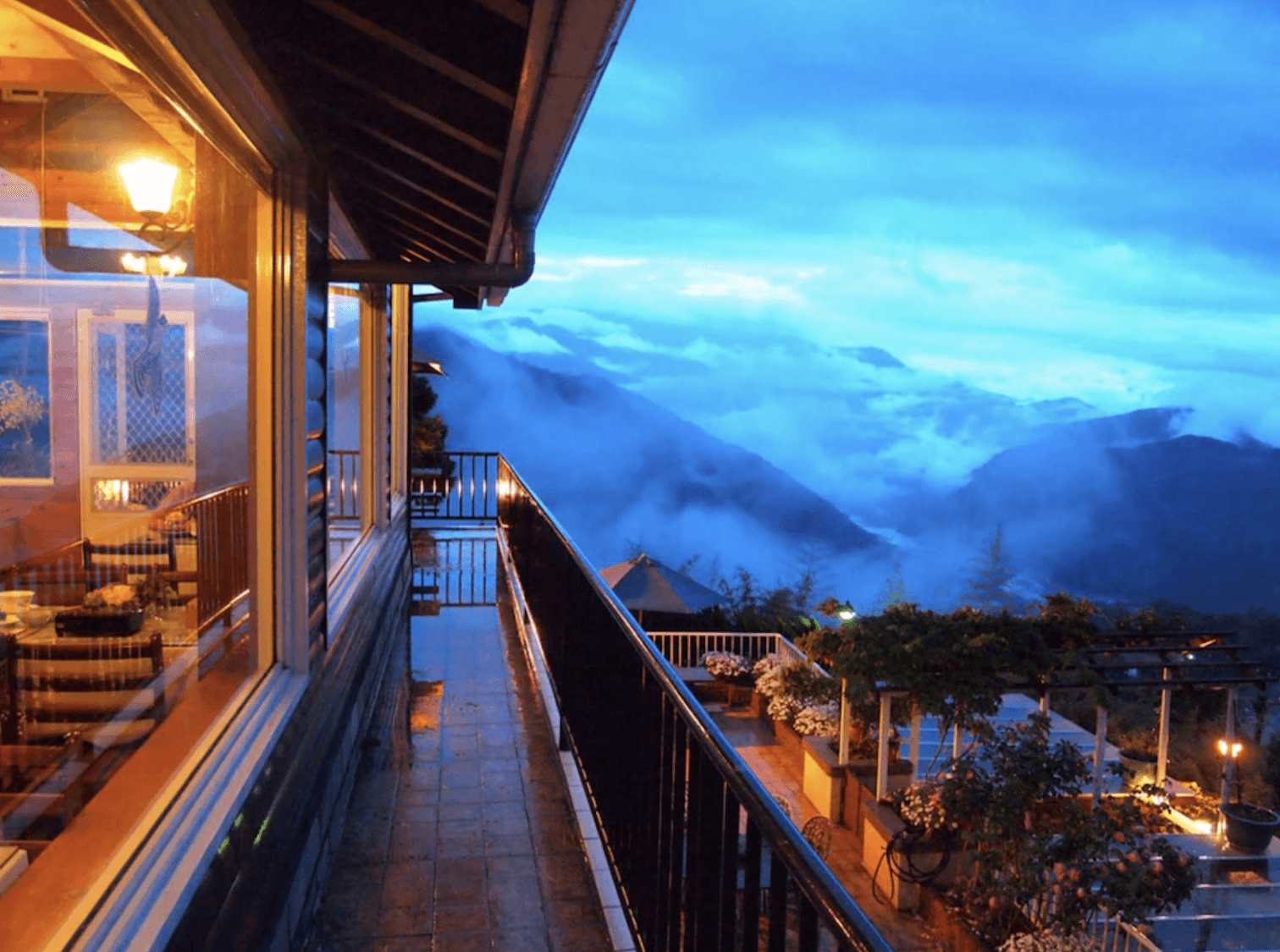 【清境農場住宿】五里坡民墅傍晚時分的山景露台，遠方雲海與層巒疊嶂交織成夢幻景緻，露台上點綴著花草與戶外傢俱，燈光溫暖，充滿浪漫氛圍，是欣賞夕陽與雲海的絕佳位置。