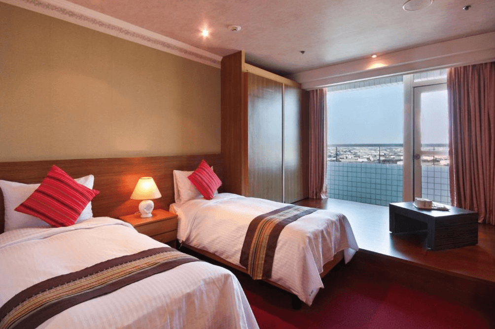 【彰化飯店】亞太鹿港渡假村雙床客房，設有兩張單人床、溫暖燈光、木質傢俱與大片窗景，窗外可眺望市區景觀。