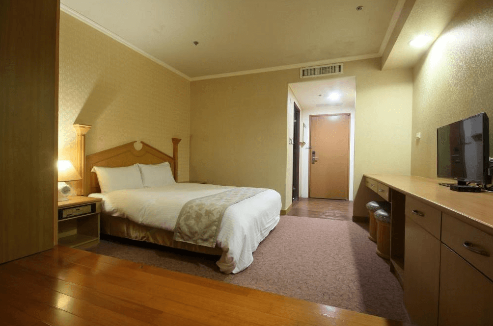 【彰化飯店】亞太鹿港渡假村雙人客房，配有一張大床、木地板與長型書桌，空間寬敞舒適並設有電視。