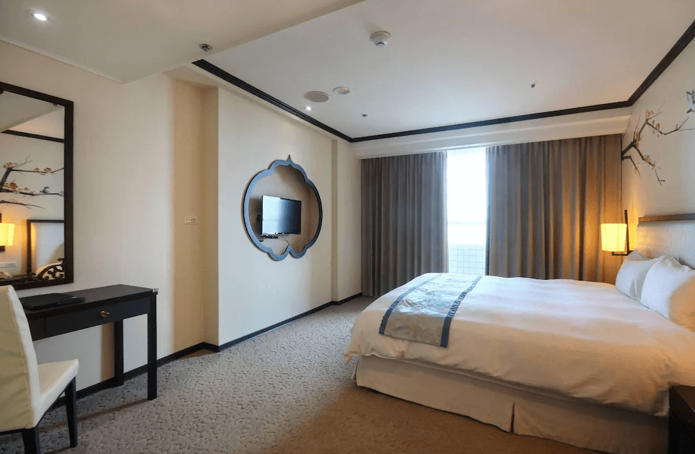 【彰化飯店】亞太鹿港渡假村典雅風格雙人房，牆面帶有東方風格裝飾，設有大床、落地窗與古典風鏡子書桌。