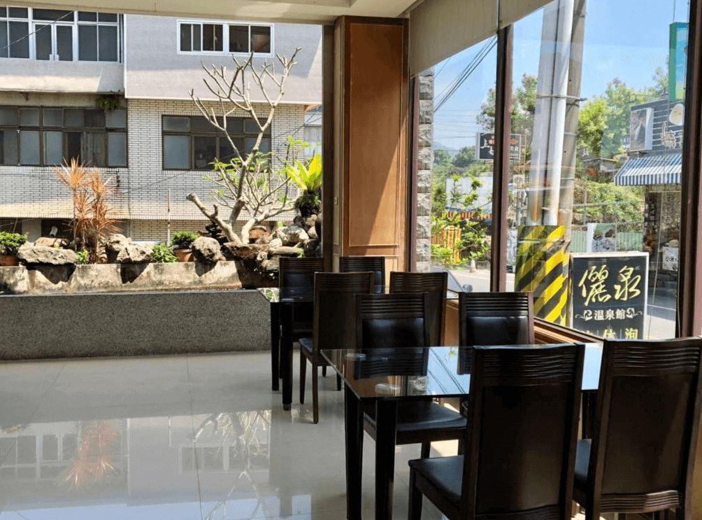 【關子嶺溫泉】“白河住宿”儷泉溫泉館的一樓用餐區設有玻璃窗與木質桌椅，可眺望街景與戶外造景區，空間明亮，適合享用早餐或下午茶。