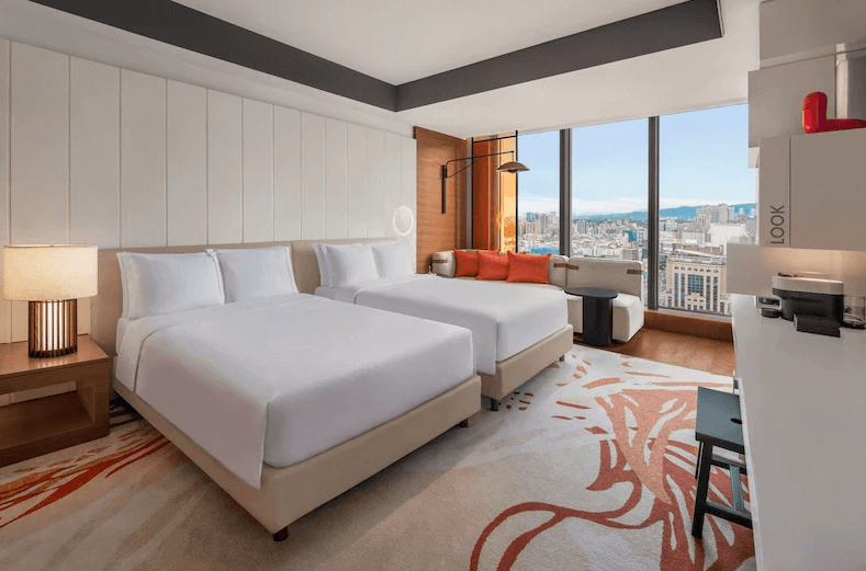 【台灣最貴飯店】台北W飯店現代時尚風格雙人客房，配置兩張舒適大床與設計感地毯，大片落地窗可俯瞰都市景致，房內設有簡約沙發與工作桌，色彩明亮富有活力。