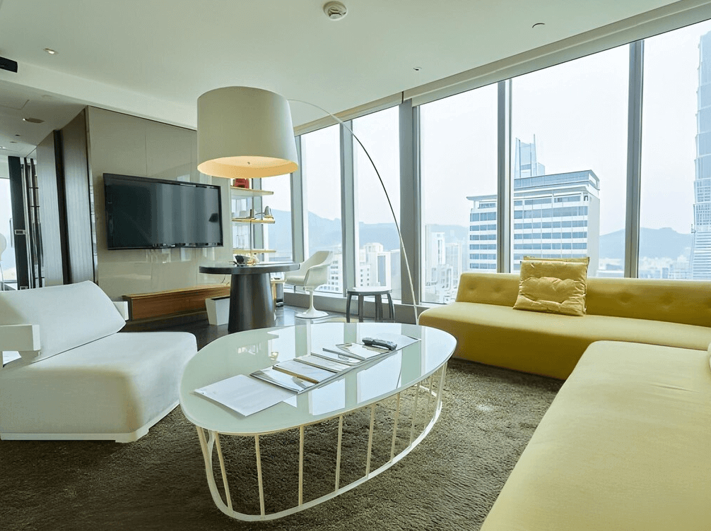 【台灣最貴飯店】台北W飯店的套房客廳區，配有造型沙發、時尚燈具與大片玻璃窗，可飽覽台北市中心高樓林立的景觀，展現W飯店獨有的摩登氛圍。