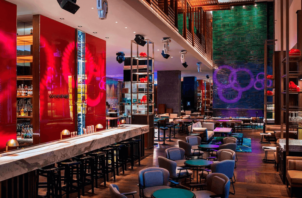 【台灣最貴飯店】台北W飯店酒吧餐廳，採挑高設計與華麗燈光，搭配紅色裝置藝術與綠色牆面，空間中充滿現代藝術與社交氛圍，為夜生活增添魅力。