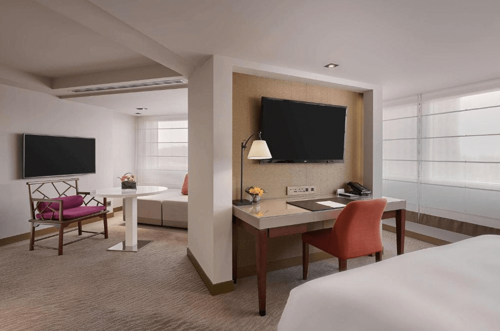 【台灣最貴飯店】台北君悅酒店的客房內設有獨立起居空間與辦公區，配置書桌、圓桌、座椅與雙電視，整體採用柔和色調與簡約設計，提供休憩與商務的多重功能。