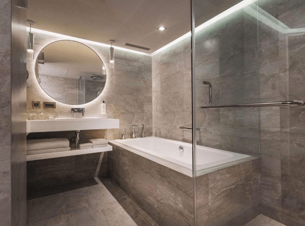 【台灣最貴飯店】台北君悅酒店以灰白石材打造的現代化浴室，設有圓形鏡面、乾濕分離淋浴間與浴缸，燈光柔和營造出溫馨放鬆的洗浴氛圍。