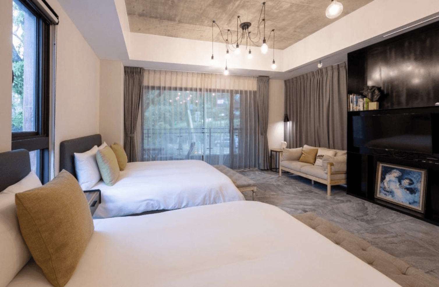 【三義住宿】向草語蟲民宿的四人房，配置兩張雙人床與小沙發，牆面設有黑色電視牆與藝術畫作，吊燈設計感十足，空間溫馨典雅。