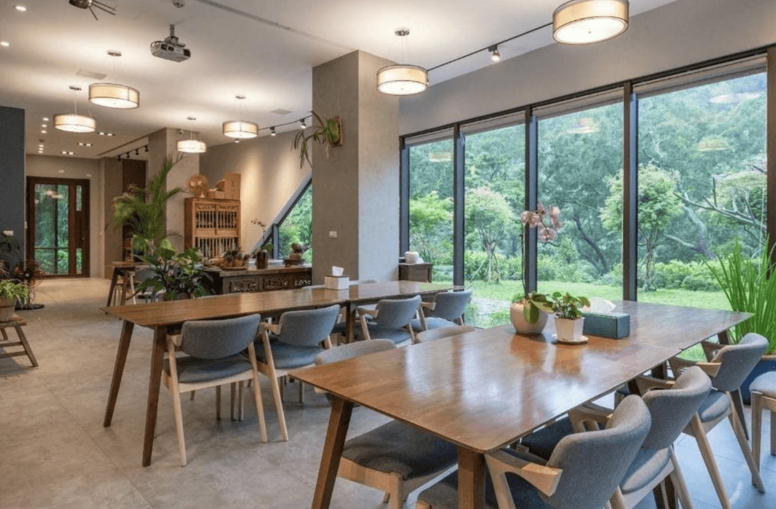 【三義住宿】向草語蟲民宿的公共用餐區，大片玻璃窗外是綠意盎然的庭園，木質長桌與灰藍色椅子營造溫馨自然的用餐氛圍。