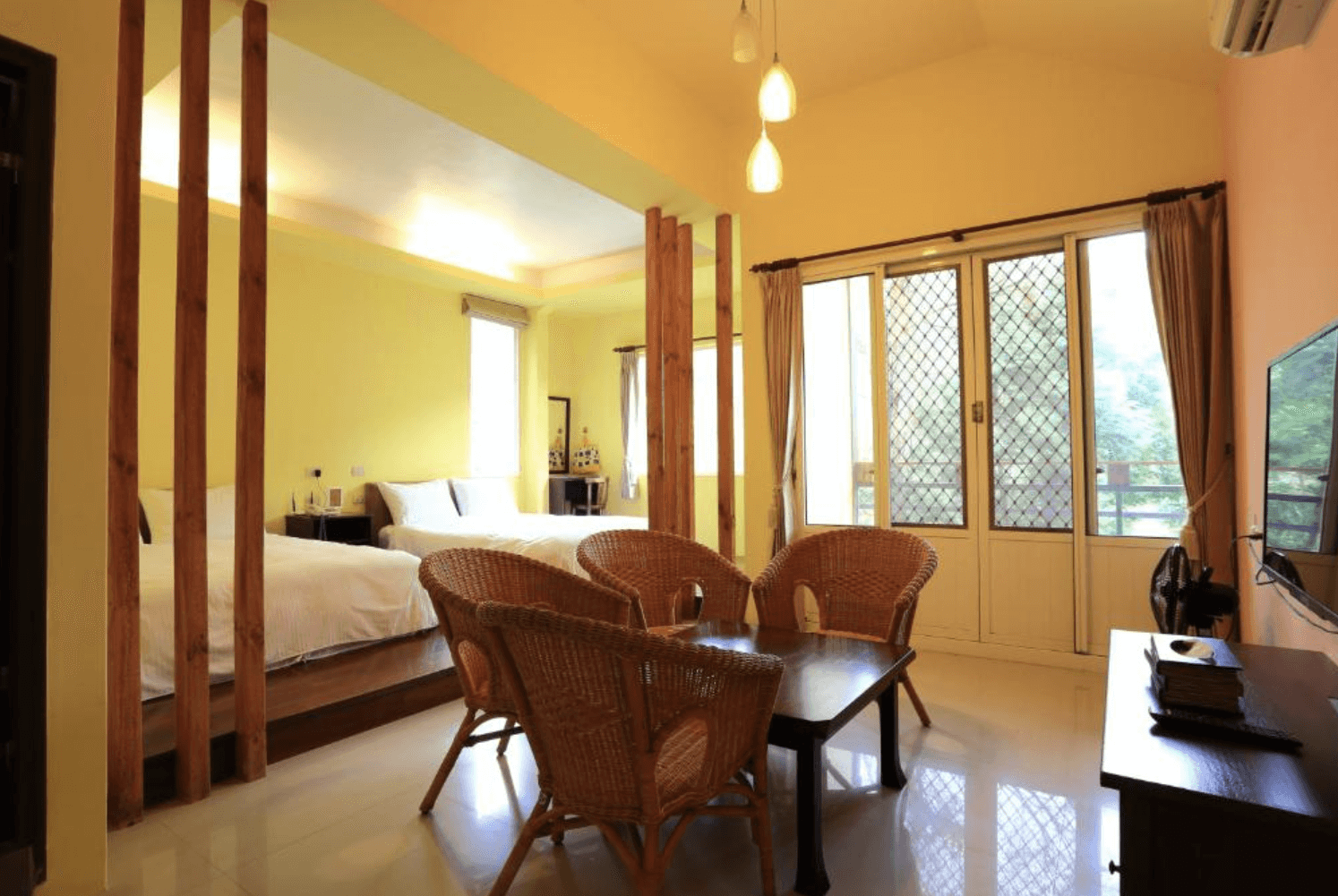 【三義住宿】向陽田園陽光通透的家庭房型，兩張雙人床設於小平台上，前方設有四人藤編座椅與咖啡桌，大片窗戶讓自然光灑入，空間舒適寬敞。