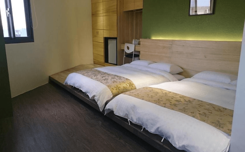 【彰化飯店】喜悅來行館四人家庭房，設有兩張加大雙人床，低床台設計搭配綠色牆面與原木風格，空間舒適寬敞。