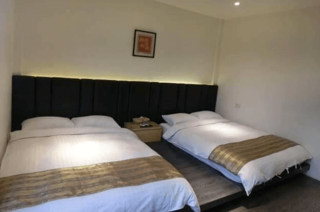 【彰化飯店】喜悅來行館四人房內景，兩張大床設於深色床背牆前，牆上裝飾簡約，採暖色調照明營造舒眠氛圍。