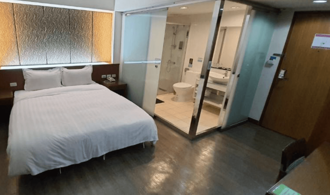 【東港住宿】大鵬灣大飯店的房間配置現代設計，床頭有燈光裝飾牆，衛浴採用透明玻璃隔間設計，空間整潔明亮，提供視覺通透感與便利性。