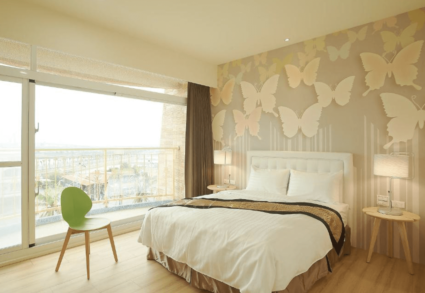 【東港住宿】大鵬灣瞭望台民宿的房間設計明亮溫馨，以立體蝴蝶裝飾牆面為主視覺，搭配木質地板與簡約家具，一旁設有大片落地窗與陽台，可遠眺大鵬灣景致。