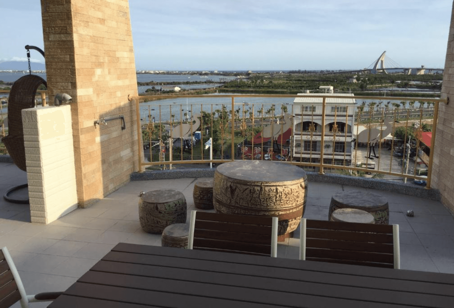 【東港住宿】大鵬灣瞭望台民宿的陽台空間寬敞，設有鼓形石桌椅與木質餐桌，可遠眺大鵬灣水岸與鵬灣跨海大橋，適合悠閒賞景與聊天放鬆。