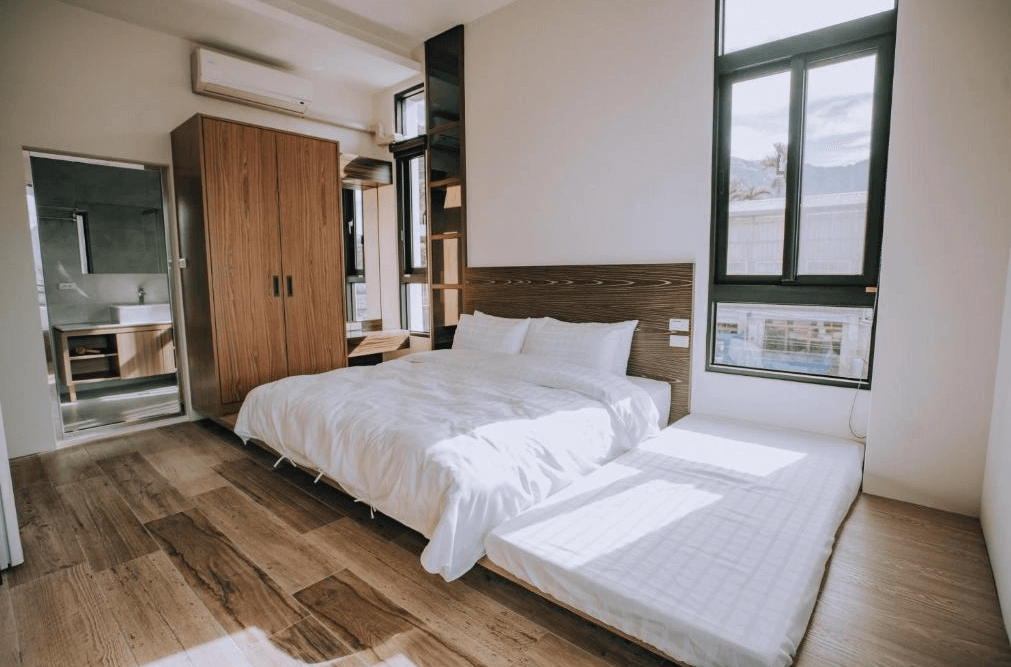 【瑞里民宿】山間茶墅民宿的現代簡約風家庭房，設有一張雙人床與一張和式床墊，大片窗戶引入自然光線，房內以原木色地板與簡約傢俱營造溫馨氛圍。