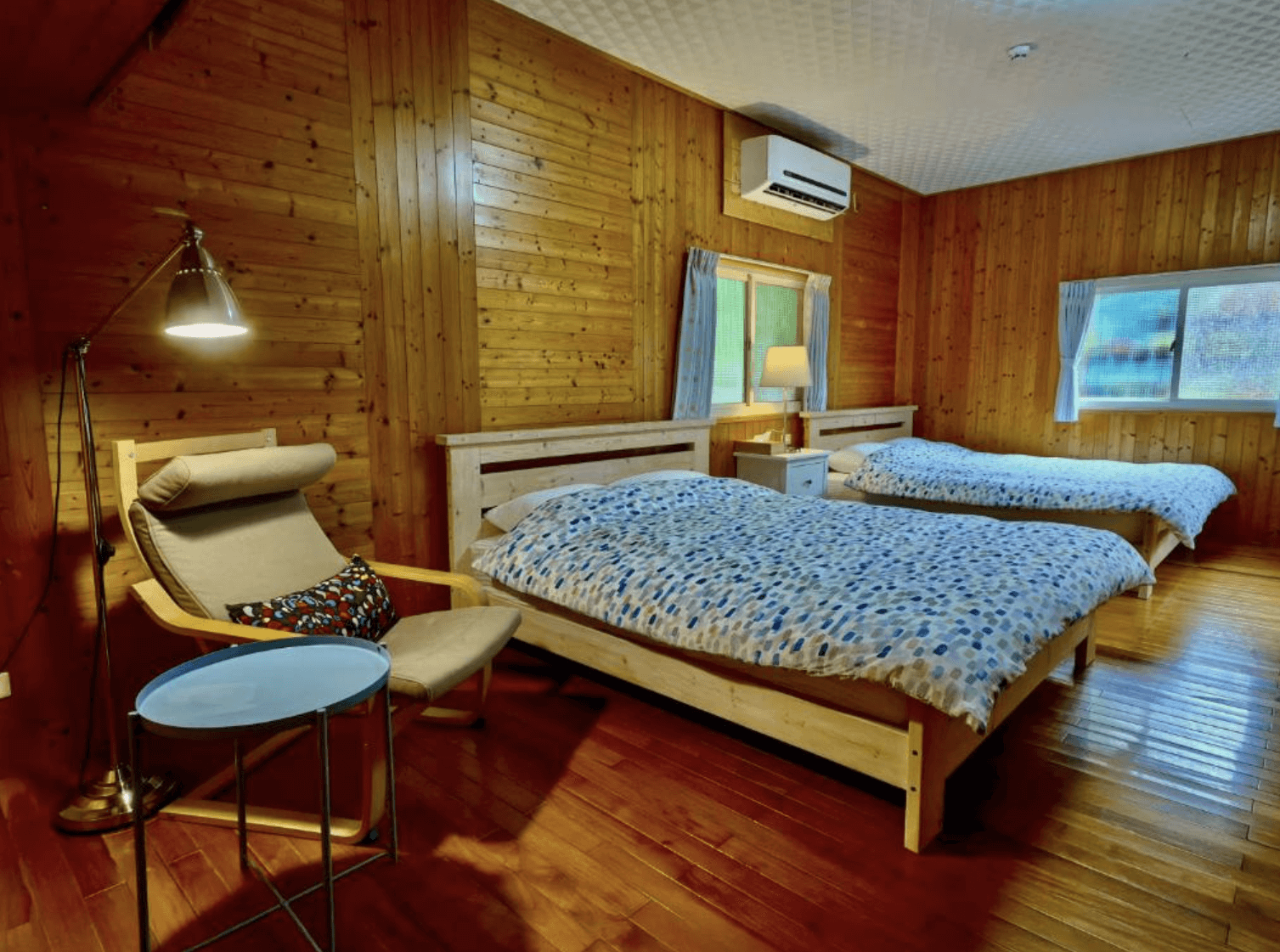 【三義住宿】峯州小木屋全木質裝潢的四人房，配置兩張雙人床與閱讀角落，設有柔軟躺椅、立燈與小茶几，展現溫暖樸實的山林小屋氛圍。