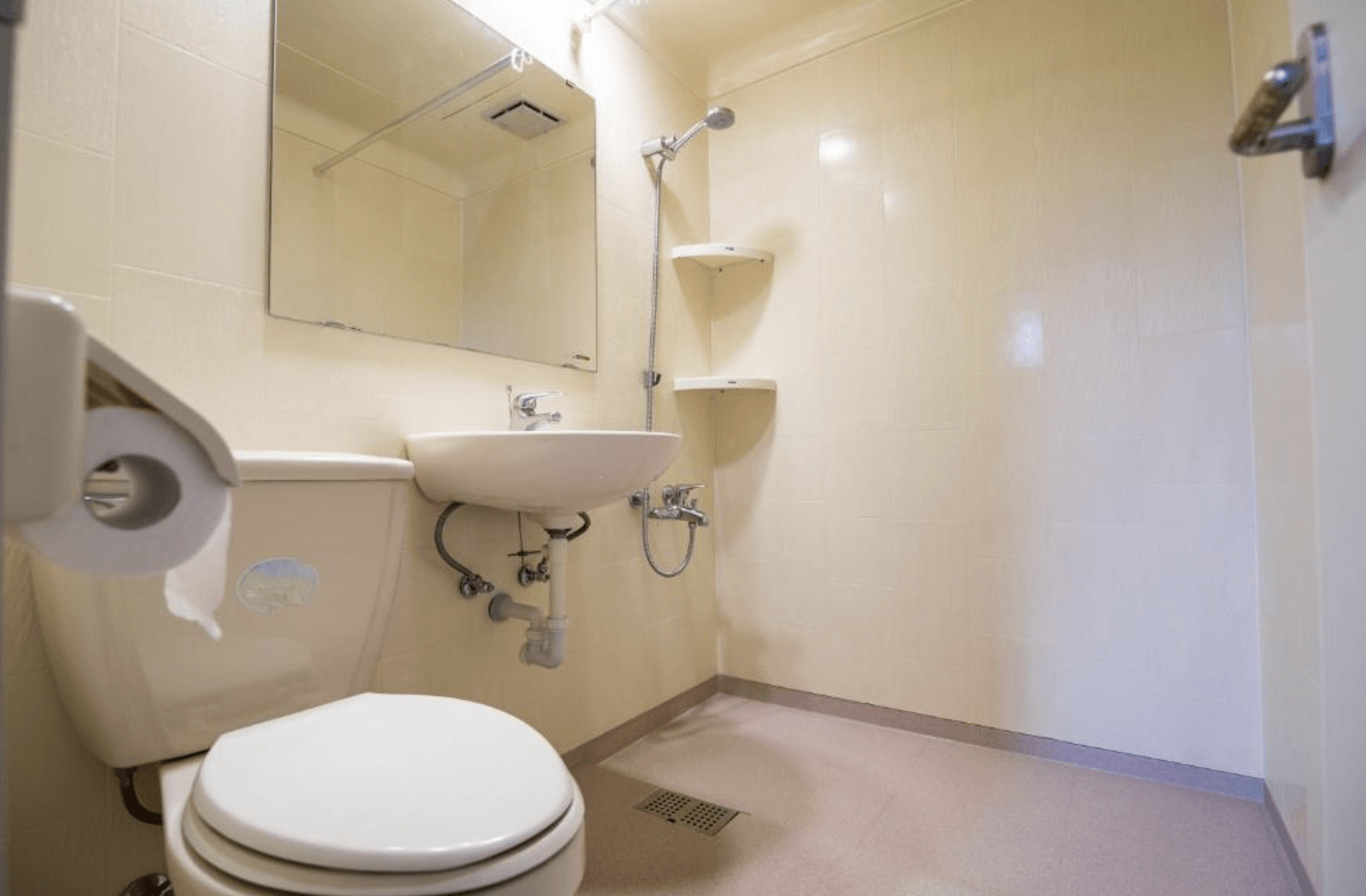 【三義住宿】峯州小木屋簡潔乾淨的衛浴空間，設有馬桶、洗手台與淋浴設備，米白色系牆面與鏡子搭配，採用無浴缸的開放式設計。