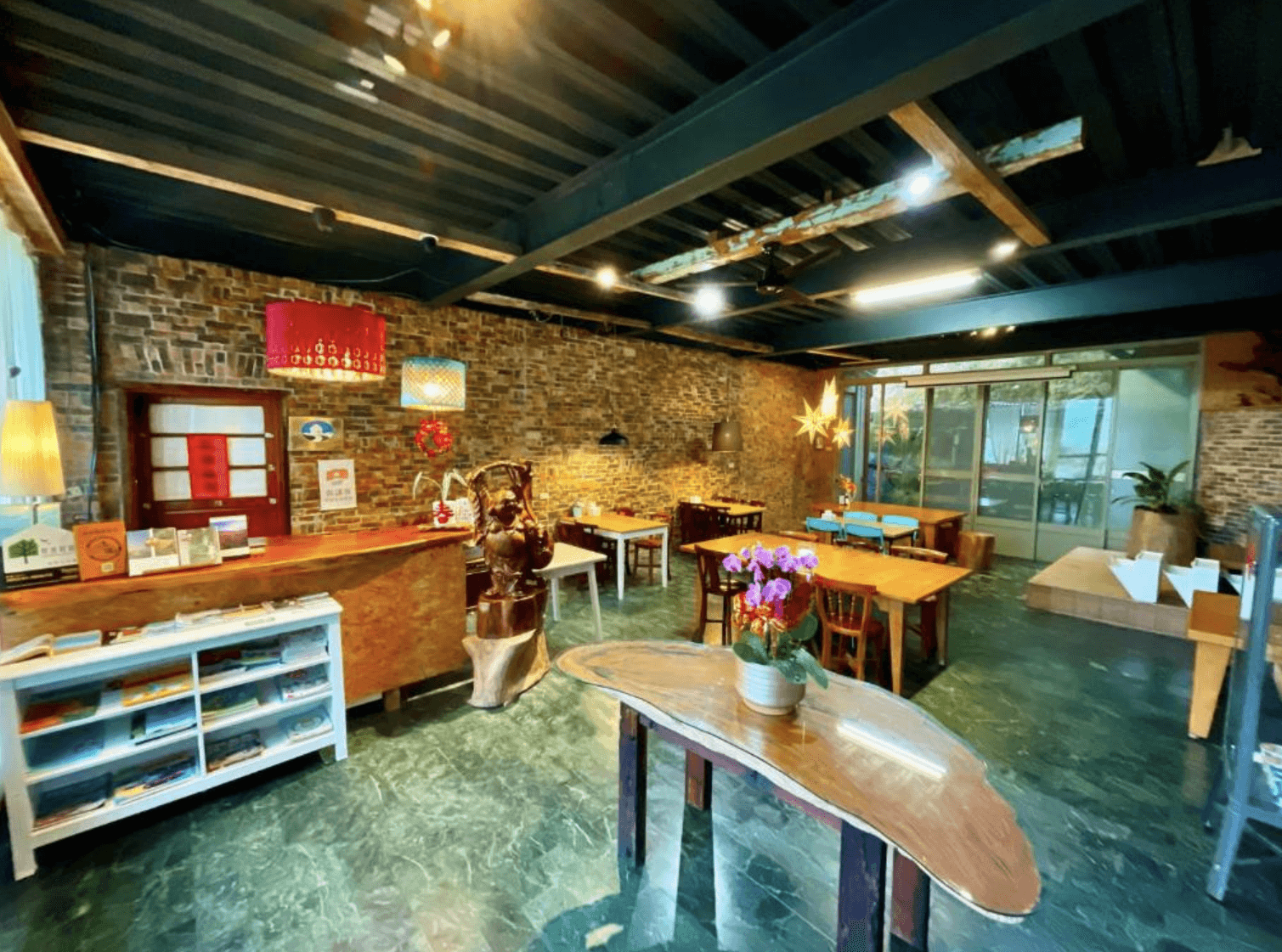 【三義住宿】峯州小木屋風格獨特的公共交誼廳，紅磚牆面搭配木質櫃台與各式桌椅，設有閱讀角、咖啡區與藝術擺設，空間氛圍溫馨又具設計感。