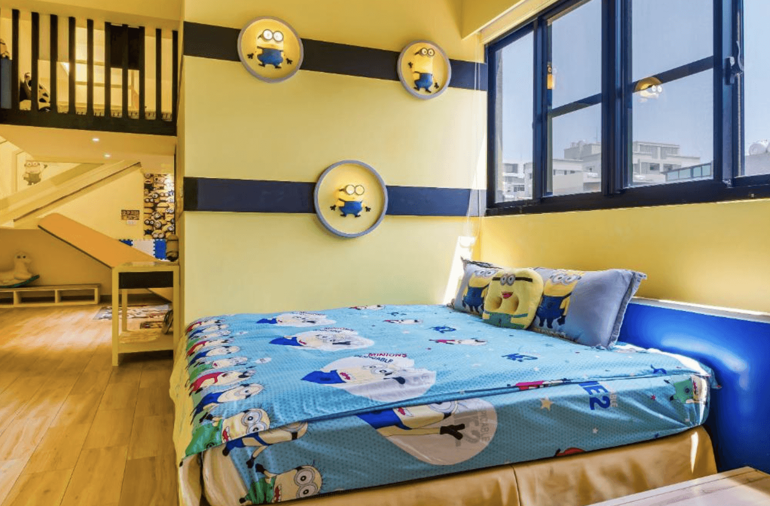 【東港住宿】幸福浪漫旅以黃色和藍色為主色調，裝飾著多個小小兵主題燈具和壁貼，床單、抱枕皆為小小兵圖案，充滿活潑氣息。房間設有上下層空間，內部有滑梯與兒童遊戲區，營造出趣味十足的親子住宿環境。