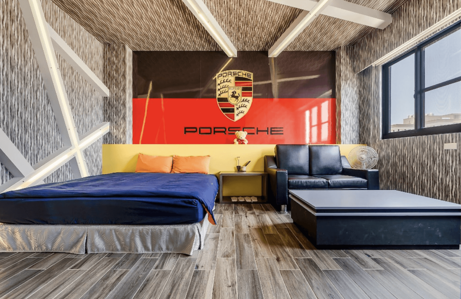 【東港住宿】幸福浪漫旅工業風格的主題房，以保時捷汽車為設計主軸，牆面上有醒目的保時捷標誌及紅黑色彩牆。房間配置簡約時尚，設有雙人床、黑色沙發、茶几及木質地板，適合汽車迷入住。