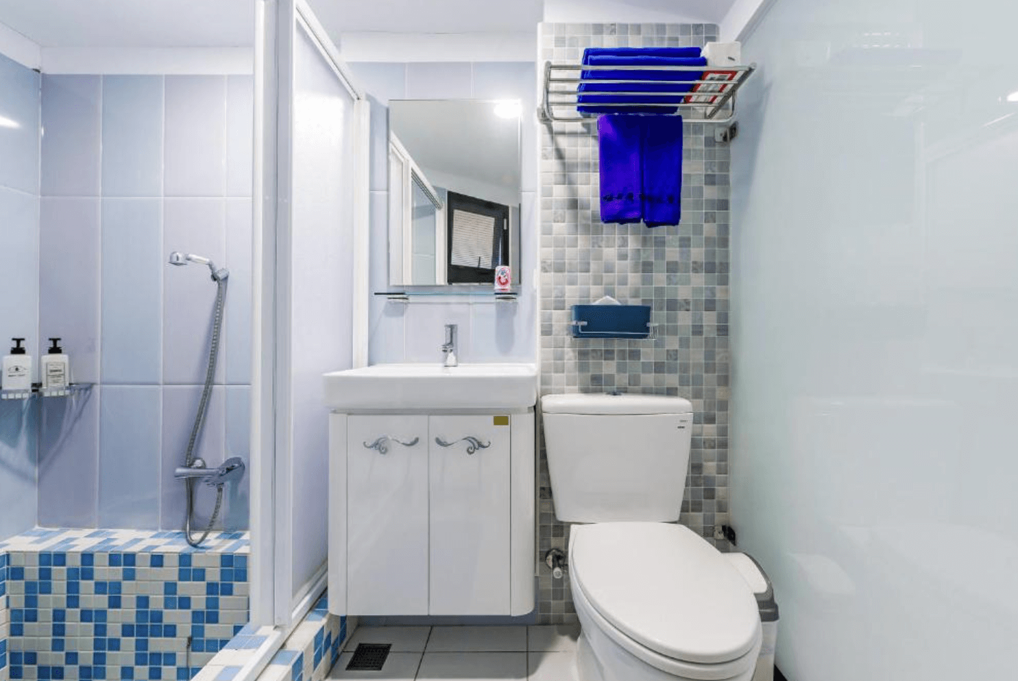 【東港住宿】幸福浪漫旅乾濕分離的衛浴空間，採用淺藍與白色系磁磚裝飾，搭配簡約風鏡櫃與洗手台，牆面設有毛巾架與衛生紙架，整體乾淨清爽、功能齊全。