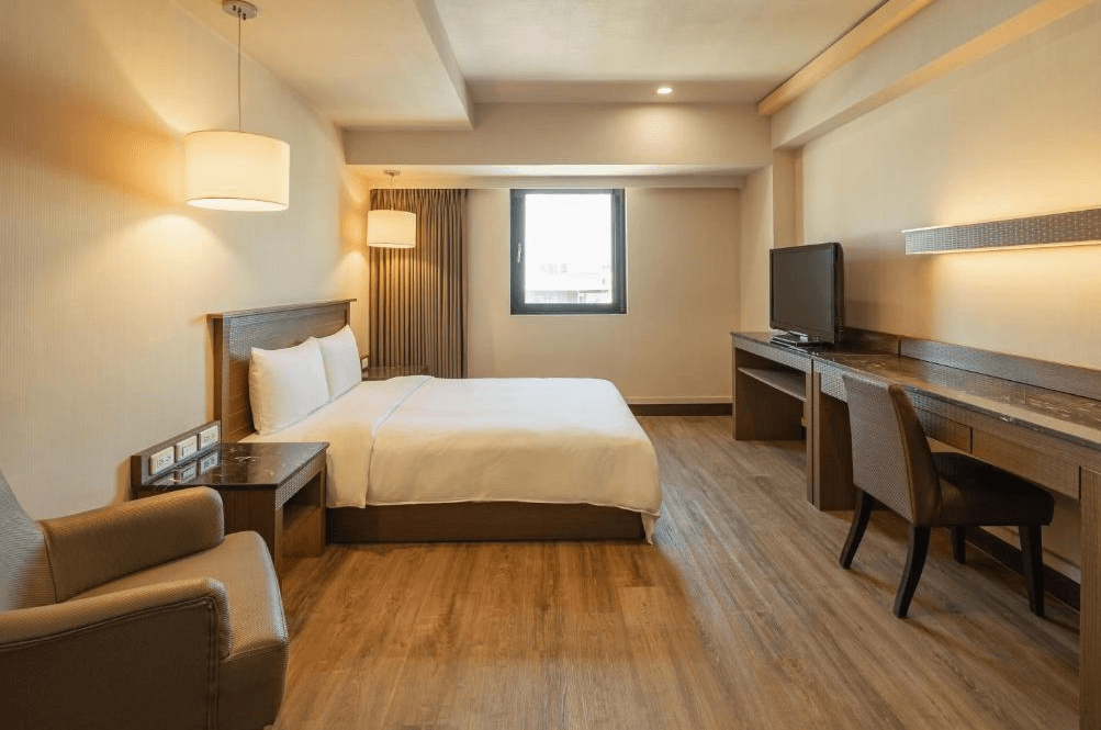 【彰化飯店】康橋商旅彰化員林館商務雙人房，設有一張大床、長書桌與電視，空間簡約溫馨，搭配木質地板與現代燈飾。