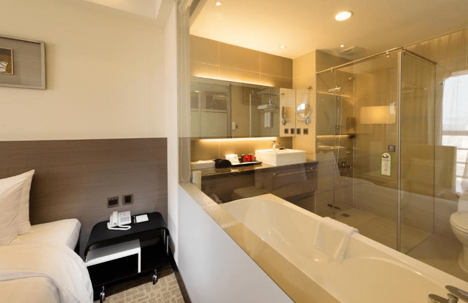 【彰化飯店】彰化福泰商務飯店房內設有開放式衛浴空間，浴缸與透明玻璃隔間的淋浴間相連，設計現代典雅。