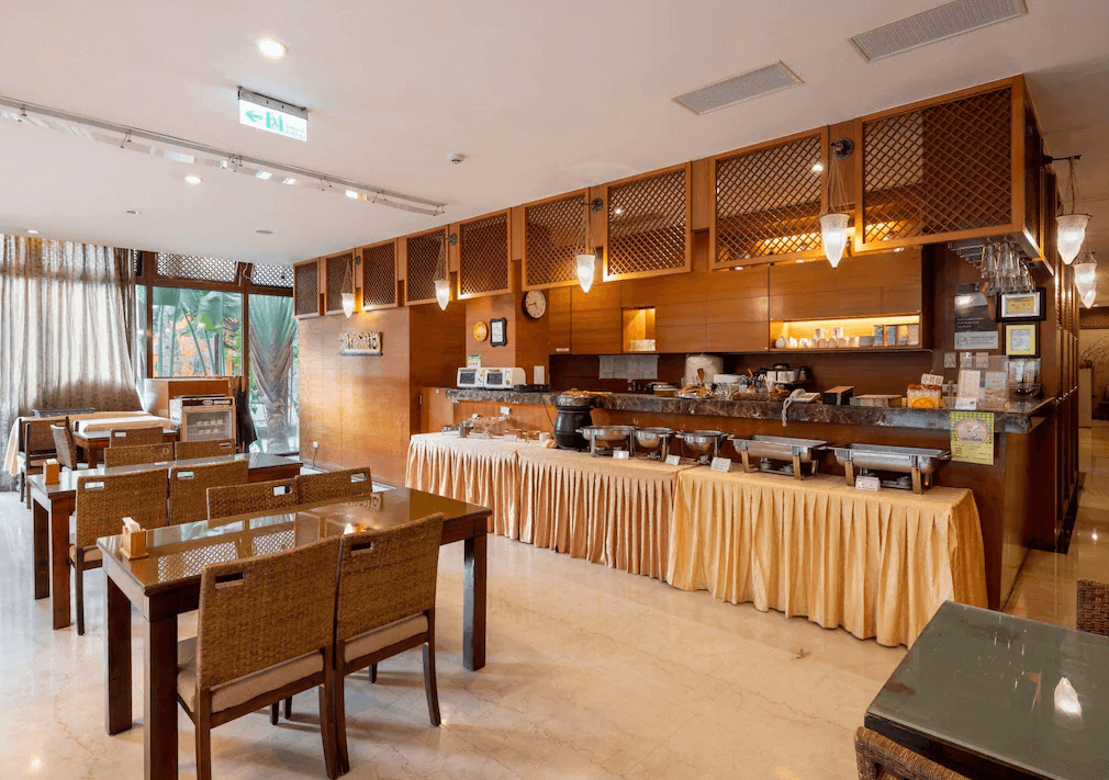 【谷關住宿】惠來谷關溫泉會館的餐廳裝潢採溫暖木質色系，擺放藤編餐椅與玻璃餐桌，空間舒適寬敞。自助餐區供應多樣熱食、飲品與麵包，檯面整潔，搭配柔和照明，早晨用餐氛圍輕鬆自在。