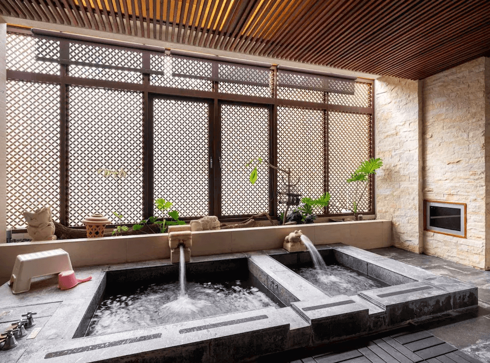 【谷關住宿】惠來谷關溫泉會館的室內設有雙水池設計，湯池以灰黑石材砌成，並配置獨立出水口與溫泉控制。大片格柵窗結合綠植與石牆，既保有隱私又能通風採光，是房客專屬的放鬆小天地。