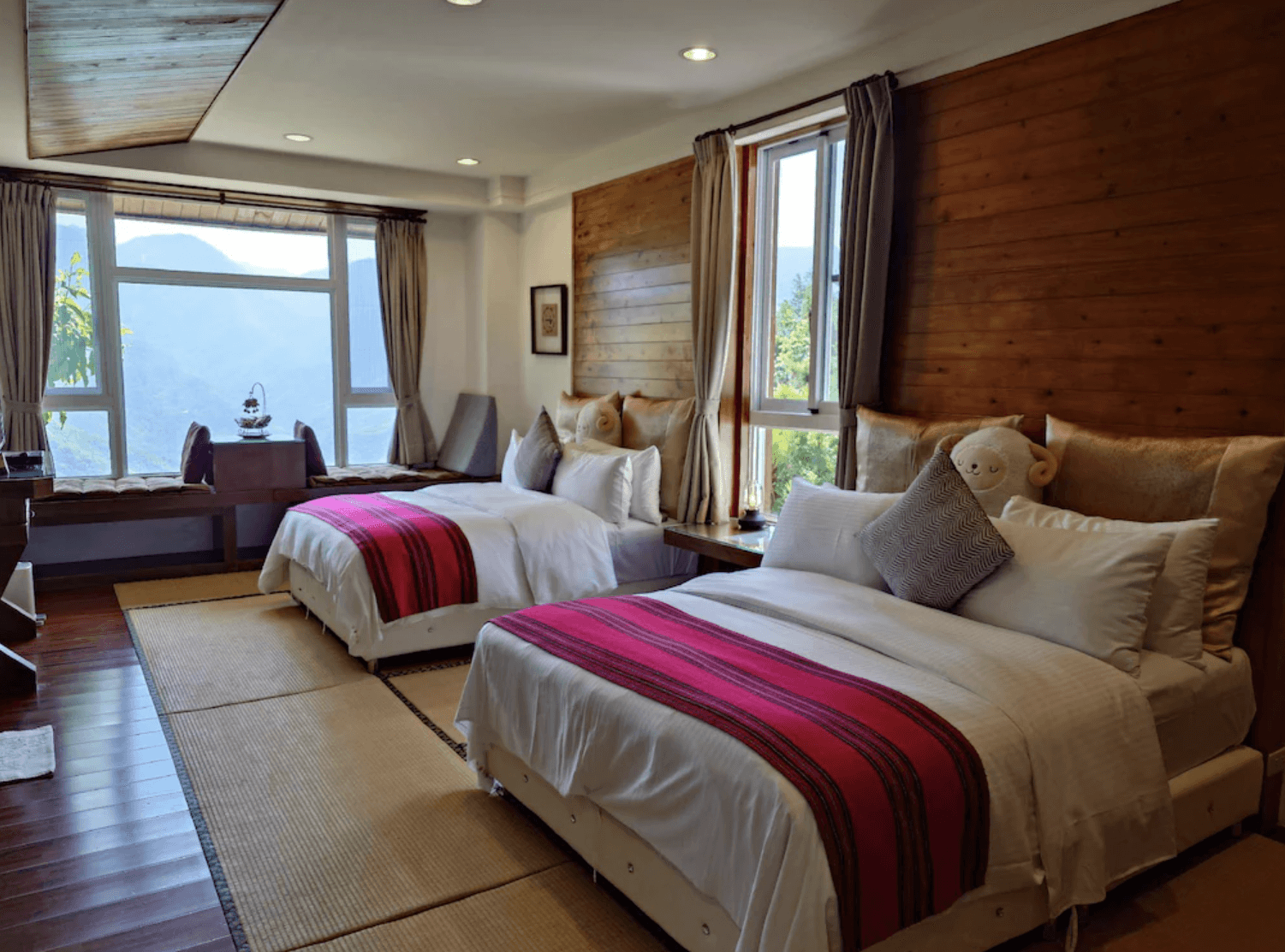 【清境農場住宿】愛薰閣會館的雙人房內部空間，搭配兩張雙人床、紅色條紋床尾巾與大型觀景窗，房內充滿自然光與山景視野。